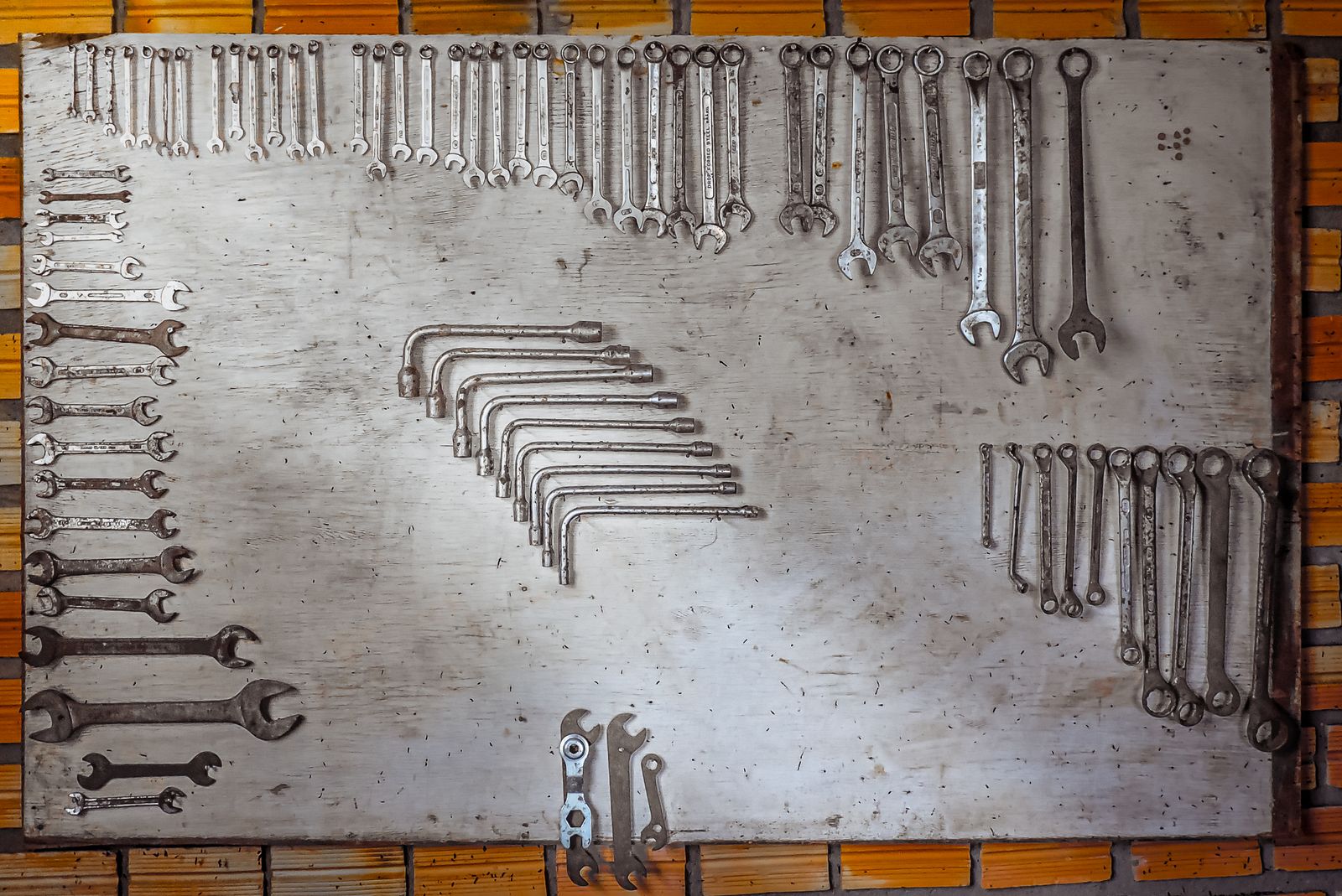 Overhead shot of a well-worn wooden pegboard with dozens of spanners, wrenches, and hex keys hung in organised rows